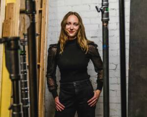 Abby posed confidently in a production studio, surrounded by professional lighting equipment, embodying her role in the video production industry at Windsong Productions.