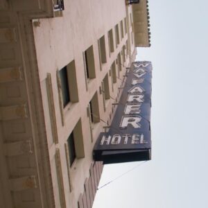 Upward view of the historic Wayfarer Hotel in Downtown Los Angeles, showcasing its vintage black neon sign against a light-colored building façade.