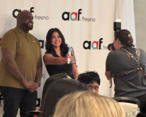 Jordan Singh posing with award presenter while photographers capture the moment at the AAF Fresno Awards.